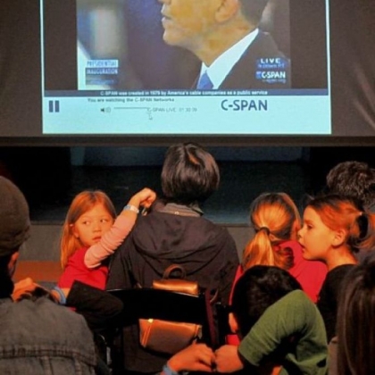 Jacqueline Chalifoux, left, and Chloe Rodrigues turn to watch the crowd during the broadcast of the ceremonial inauguration in the theater at the Children's Museum of Pittsburgh.
