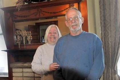 Cathy and George Lewis, owners of the Wigman house in Carrick, in front of one of the ornamental wooded mantels, this one in the dining room.