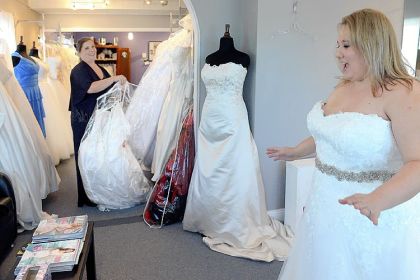 Co-owner Mary Beth Ryfun, left, helps Medina Menozzi try on wedding gowns at Koda Bridal in Mt. Lebanon. Ms. Menozza says she plans to be early for the military brides gown giveaway.