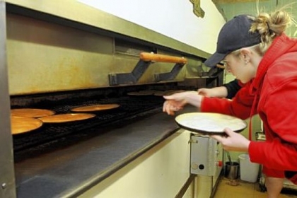 Alex Hill loads pizza crusts into the ovens at Augustine's pizza in New Castle, which makes between 2,400 and 3,000 crusts per day. The pizza is now sold at PNC Park, Giant Eagle and other venues.