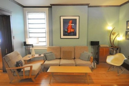 Heywood-Wakefield furniture fills the sky blue living room. The light fixture is a spaghetti lamp with shades made of spun resin. Above the sofa is a Charles Biddle photograph of a neon sign for the Parkwood Inn in Greensburg. At right is an Eames rocker.