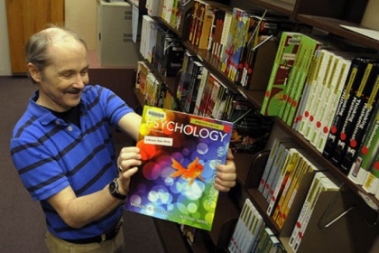 Bruce Johnston, access services librarian, holds one of about 200 textbooks that are on reserve at the Robert Morris University library. It has allowed about one in five students to access required textbooks without buying them.