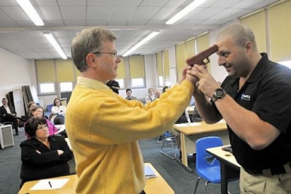 In this three-photo sequence, Sam Rosenberg, black shirt, shows North Catholic High School religion teacher Greg Evans, left, how to disarm a gun-wielding intruder at close range during a session at the Troy Hill school on Monday.