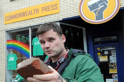 Dan Rugh, owner of Commonwealth Press, with the brick that broke a front window (since fixed) at his East Carson Street business.