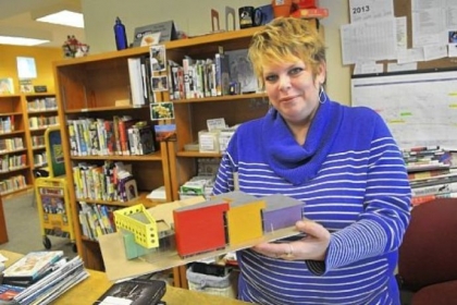 Jamie Cozza, a circulation assistant, displays a model of the planned renovation to the library building in Sharpsburg. It is expected to double in size following the receipt of a large state grant. The brown section is the existing structure.