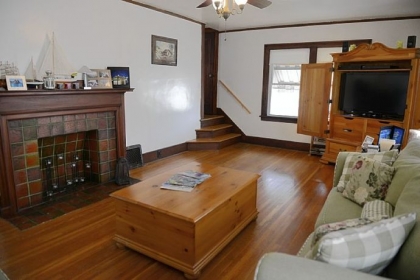 The living room in this two-story Colonial in Washington has a hardwood floor. The decorative fireplace has an original tile surround and hearth topped by a beautiful Craftsman-style wood mantel.